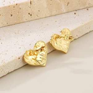 Macro di orecchini a cuore placcati in oro con texture martellata su travertino