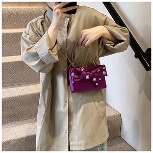 Detail of luxury purple velvet clutch bag with crystal bow and gold chain on model