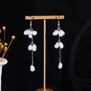 Close-up of pearl tassel earrings with silver hooks on a premium black background