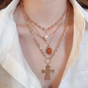 Macro shot of layered gold cross necklace with pearl and ruby pendant accents