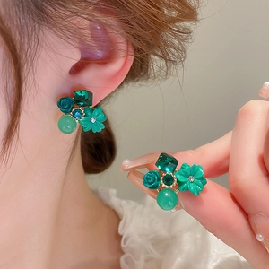Detailed view of green crystal flower earrings with feline cat eye stones on model