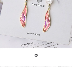 Macro shot of gradient wing earrings with pearl accents on a white jewelry display card