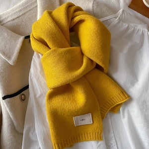 Detailed texture of bright yellow knitted scarf with 'emo' logo on beige coat