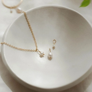Macro detail of natural white freshwater pearls and 14K gold plated necklace in ceramic bowl
