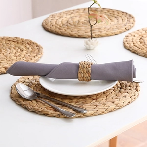Detail of hand-woven water hyacinth napkin ring with grey cloth napkin on ceramic plate
