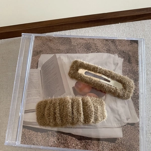 Close-up of two brown plush hair clips set on a vintage CD case and book background