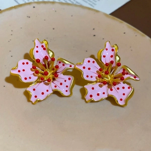 Detailed macro view of floral stud earrings with pink enamel, red dots and golden edges