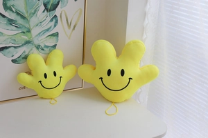 Detail view of yellow plush palm pillows with embroidered smiley faces in two sizes