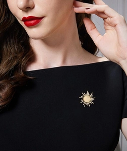 Detailed view of a gold sunburst brooch with opal and crystals on black fabric