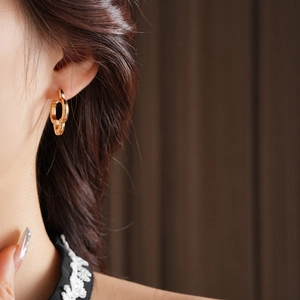 Close-up of gold hollow clover hoop earrings worn by a model with elegant metallic finish