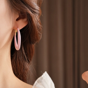 Detail shot of a model wearing large matte pink resin hoop earrings in a minimalist style