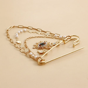Detail view of gold safety pin brooch with layered chains, pearls, and evil eye pendant