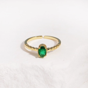 Detail view of gold open ring with an oval green stone on a textured stone base