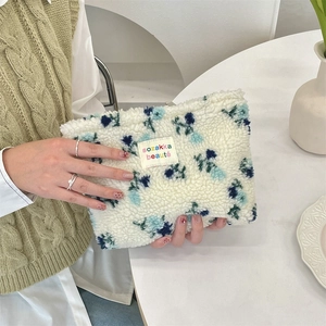 Detail of plush floral cosmetic bag with blue flower pattern held by hands