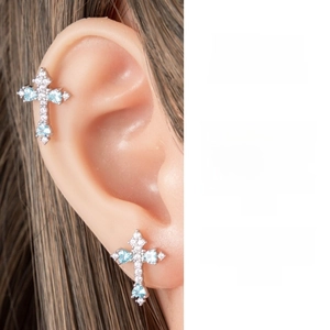 Detail of silver cross ear piercing with light blue zircon and white stones