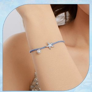 Blue woven bracelet with starfish charm and white pearl shown on a wrist
