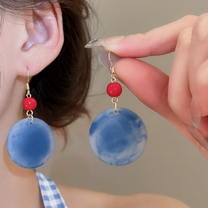 Détail de boucles d'oreilles rétro en acrylique avec disque marbré bleu et perle rouge