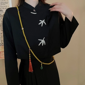 Détail d'un long collier de perles avec pompon rouge et pendentif en jade sur tissu