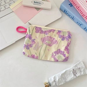 Floral fabric coin purse with pink handle shown on a desk with lifestyle accessories
