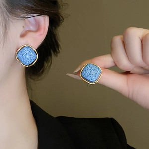 Gros plan sur les boucles d'oreilles carrées motif marbre bleu et monture dorée élégante