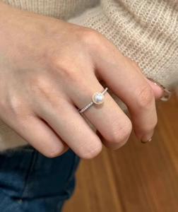 Close-up of a silver ring with a large round freshwater pearl and pavé diamonds on a hand