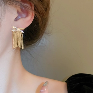 Detailed view of long gold tassel earrings with zircon X-shape on a female model