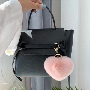 Black leather handbag with a pink leopard plush heart keychain accessory in soft lighting