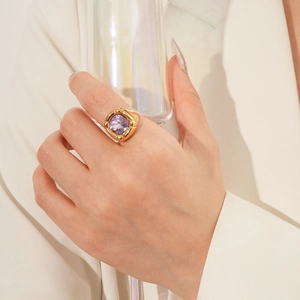 Dettaglio di un anello d'oro vintage con zircone viola su mano che tiene un bicchiere