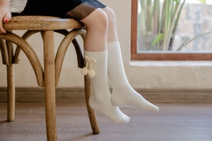 Detail of white knee-high baby socks featuring ribbed cotton texture and cute pom-pom bows