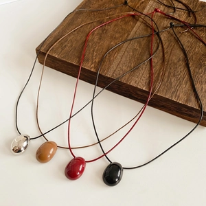 Gros plan de pendentifs minimalistes en forme de galets en argent, brun et bordeaux