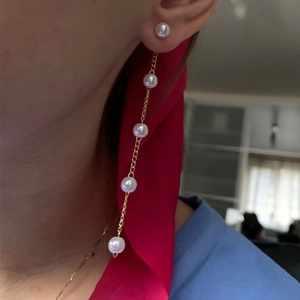 Close-up of long gold chain tassel earrings with five white pearls worn by a model