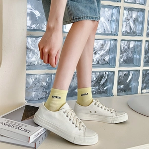 Close-up of yellow cotton socks with Smile embroidery worn with white canvas shoes