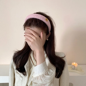 Dettaglio del cerchietto imbottito in tweed rosa con logo dorato sulla modella