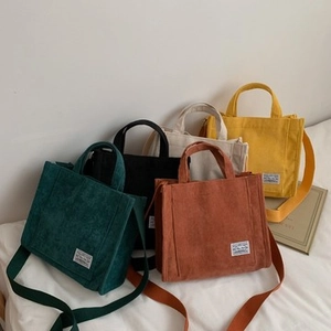 Group display of corduroy tote bags in five colors with ribbon handles and crossbody straps