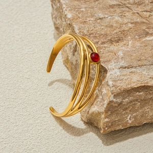 Dettaglio del bracciale multistrato dorato in acciaio inossidabile con pietra rossa tonda