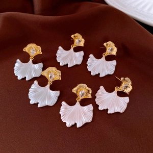 Detailed view of golden ginkgo leaf earrings with white enamel and sparkling zircon accents