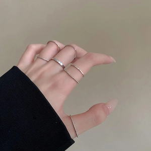 Detailed view of seven minimalist silver stacking rings styled on fingers over dark sleeve