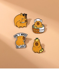 Lot de quatre broches capybara en émail aux poses variées sur un fond beige neutre