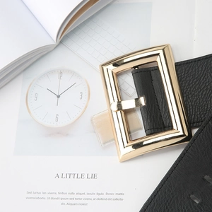 Macro detail of black litchi texture belt featuring a large golden rectangular metal buckle