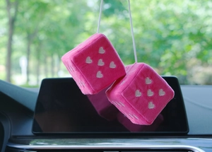 Close-up of pink plush car dice with white heart patterns hanging on a rearview mirror
