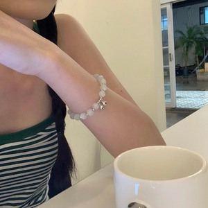 Primer plano de una pulsera de cuentas blancas con colgantes de cascabeles de plata