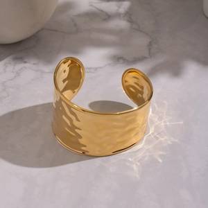 Minimalist wide hammered open bangle in 18K gold stainless steel on marble surface