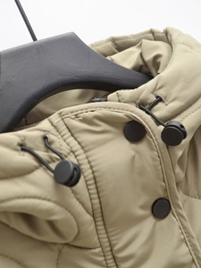 Detail of matte black snap buttons and drawstring toggles on olive green hooded jacket