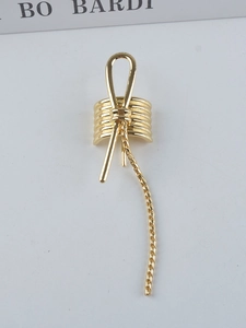 Detail of a gold metal hair clip featuring a bow design and long twisted tassel chains