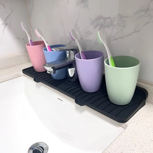 Detail of black silicone faucet mat with toothbrushes and cups on a marble countertop
