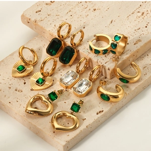 Close-up of gold titanium steel earrings with heart-shaped emerald zircon on travertine