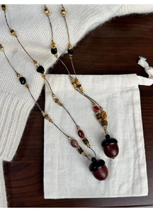 Close-up of vintage beaded acorn pendant necklaces and a linen pouch on a knit sweater