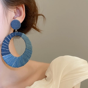 Detailed close-up of blue denim fabric wrapped oval drop earrings on model