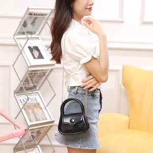 Glossy black PVC jelly handbag with gold chain strap carried by a model in a cozy room