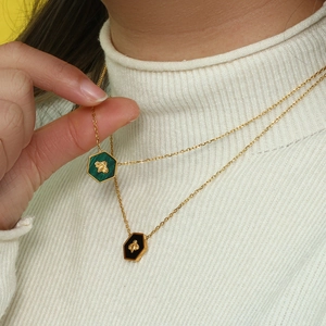 Detail of green and black hexagonal bee pendants on gold necklaces worn by model